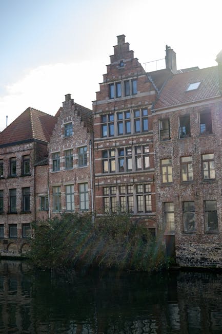 An exterior view of a multi-storey residential building constructed of red brick with a tiled pitched roof and multiple white-framed sash windows. In the foreground, two individuals are walking on the